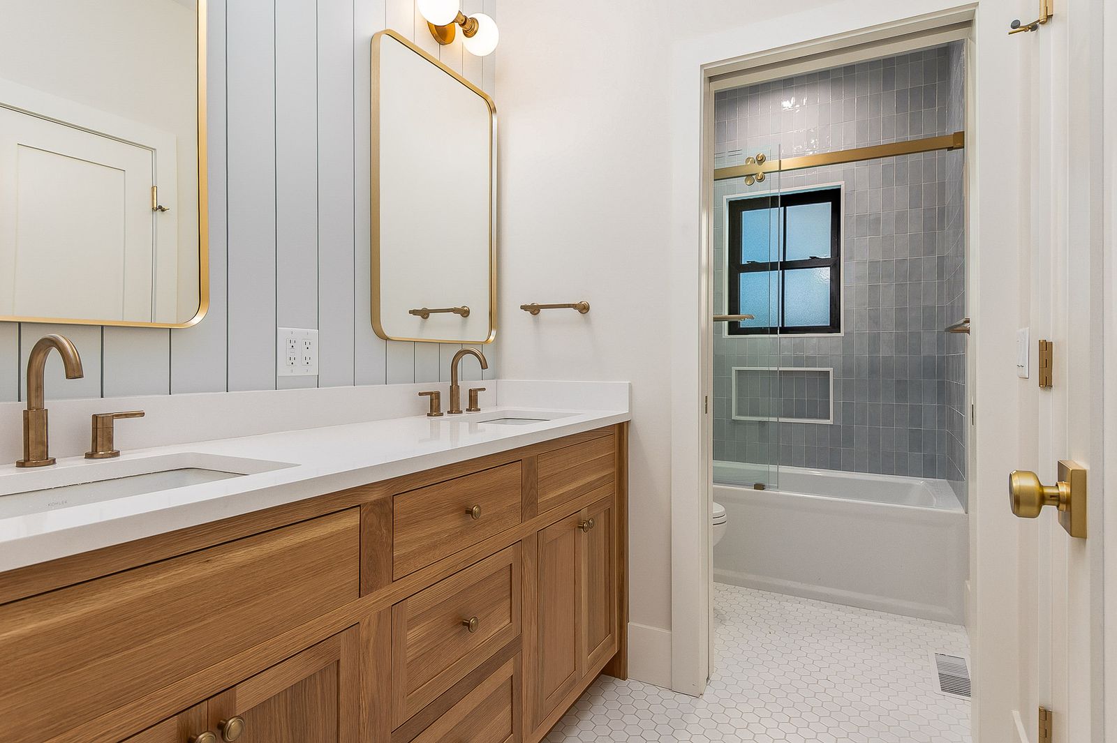 Bath with an oak vanity, brass-framed mirror and a tiled tub alcove - a River Birch Builders home in the New Hampshire Seacoast
